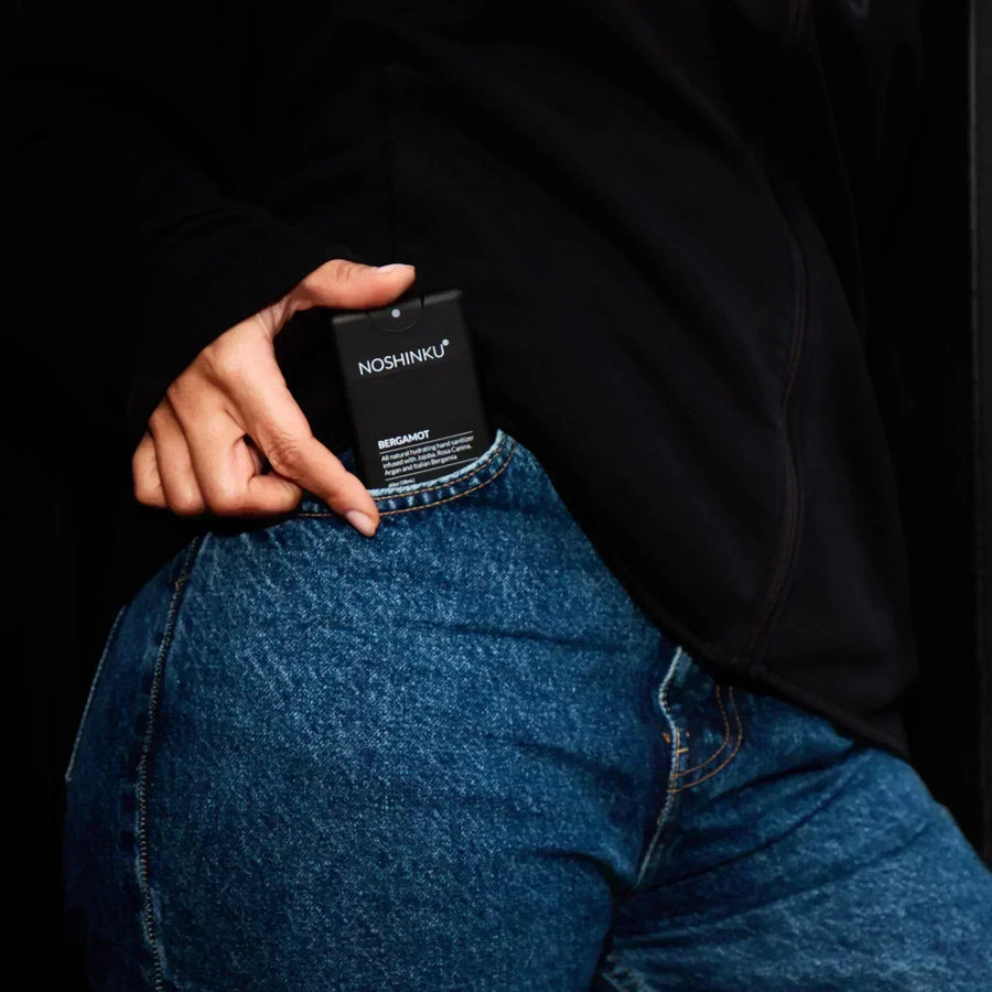 Hand sliding a black Noshinku Bergamot hand sanitizer spray bottle into a pair of denim jeans.