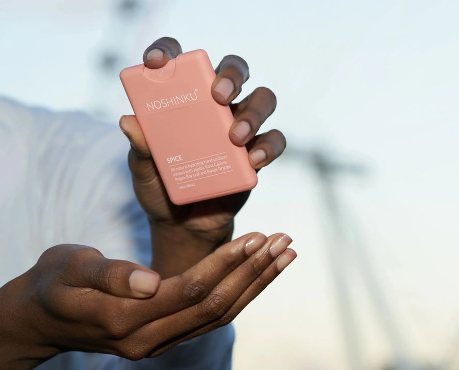 A hand holding and spraying a Noshinku Spice pocket hand sanitizer above cupped palms.