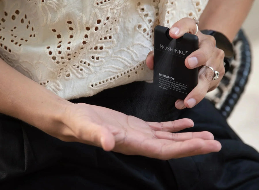 Person spraying a black Noshinku Bergamot hand sanitizer bottle onto their open palm.