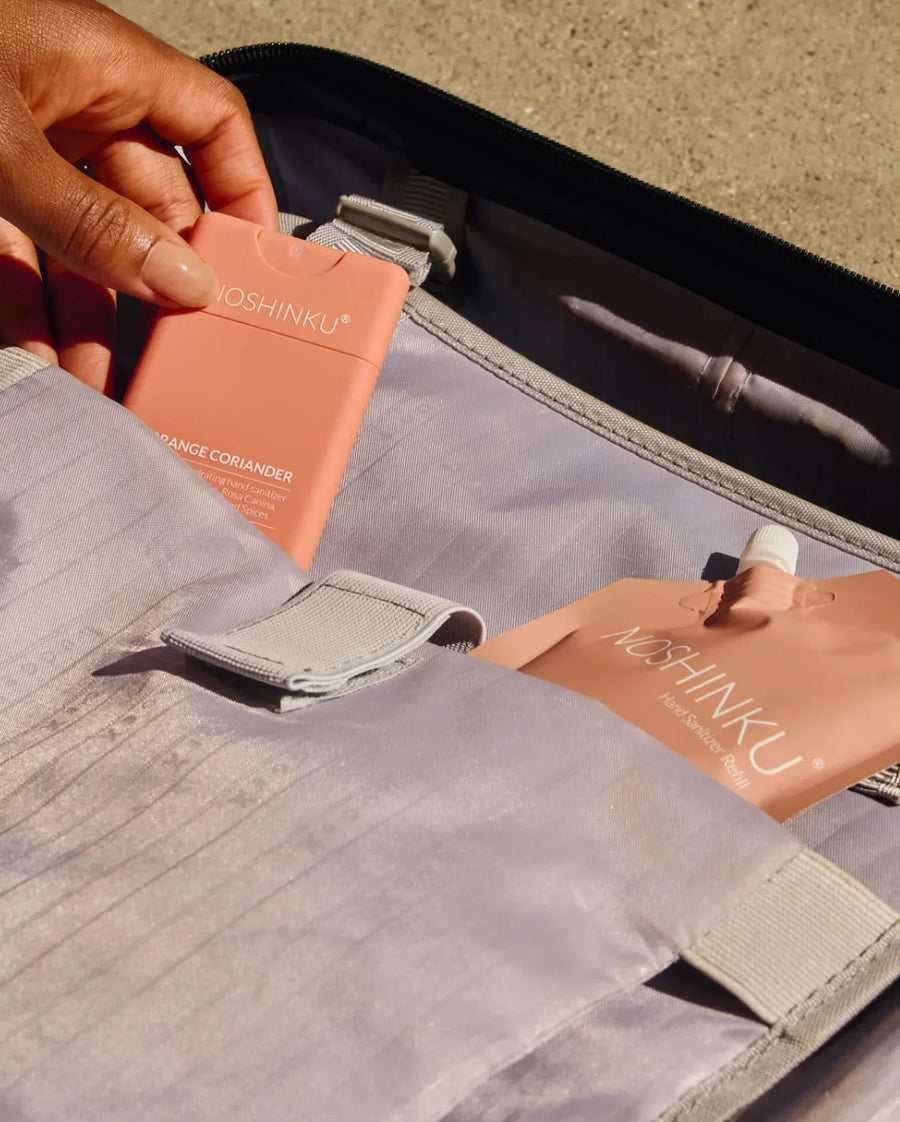 Hand placing a compact Noshinku Orange Coriander hand sanitizer into a backpack alongside a refill pouch.